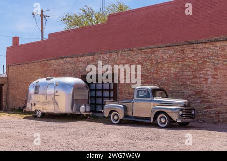 Silver painted classic fort pickup truck and a stainless steel Airstream camper travel trailer parked in downtown Winslow Arizona Stock Photo