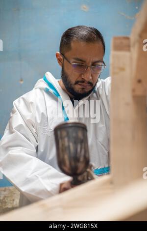 young man using lacquer gun for painting, craft work tools on furniture, industrial factory and objects at workplace, lifestyle Stock Photo