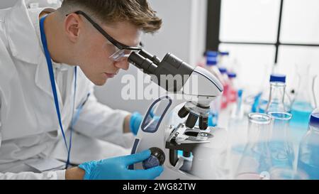 Handsome young caucasian man, a dedicated scientist, deeply engrossed in analyzing samples under the microscope at a professional medical lab. Stock Photo