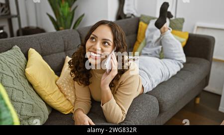 Smiling woman talking on phone while relaxing on a sofa in a cozy living room, portraying a casual, comfortable lifestyle. Stock Photo