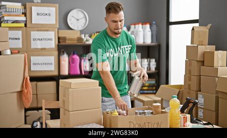 A focused man, classified as latino, volunteers at a warehouse sorting canned goods for donations amid cardboard boxes. Stock Photo