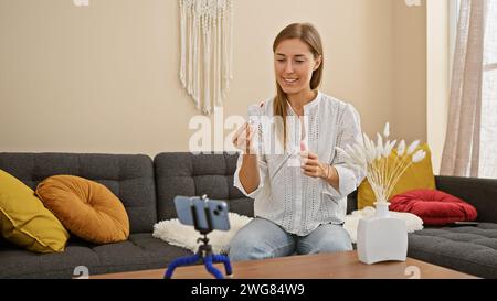 Caucasian woman vlogging at home, recording a makeup tutorial in a cozy living room setting. Stock Photo