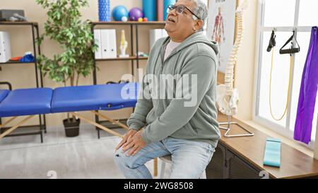 A mature man experiencing discomfort sits in a rehab clinic, showcasing healthcare in an indoor setting. Stock Photo