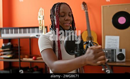 Beautiful african american woman, confident, smiling musician, wearing braids, performing indoor concert. singing song using mic in music studio, her Stock Photo