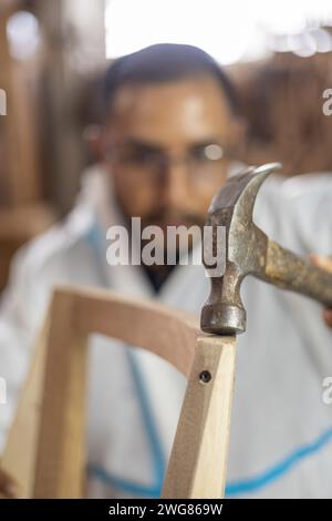 details of the construction of wooden furniture in factory interior, young man using a hammer to repair, lifestyle of artisan worker in carpentry Stock Photo