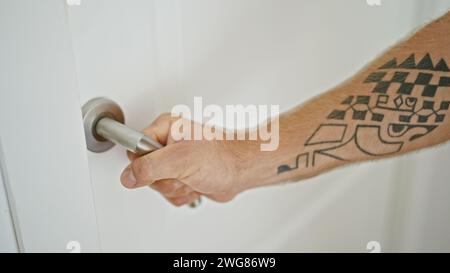 Close-up of a tattooed man's hand turning a door knob inside a bright home environment. Stock Photo