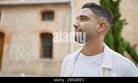 Handsome young man with a beard smiling outdoors in a city, exuding confidence and style. Stock Photo