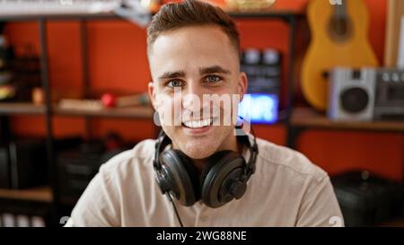 Smiling young man with headphones in music studio surrounded by musical instruments and audio equipment. Stock Photo