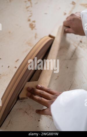 work in carpentry, detail of the hands of a person with a piece of wood sanding on an industrial machine, workplace and industry, wooden details Stock Photo