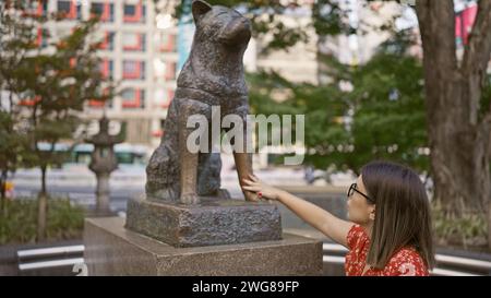 Alluring hispanic woman with glasses touches iconic hachiko statue on busy tokyo street – immersed in japanese culture and traditions Stock Photo