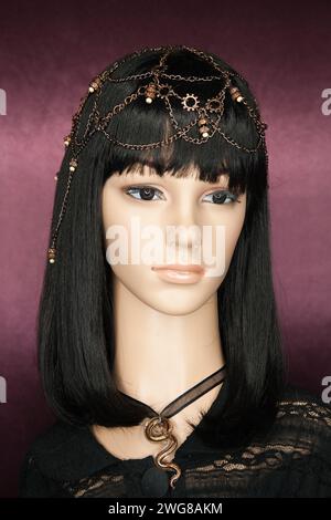 Plastic woman mannequin with long black hair wearing a chain head piece with beads, and a black lace on a purple background. Ring light catchlights in Stock Photo