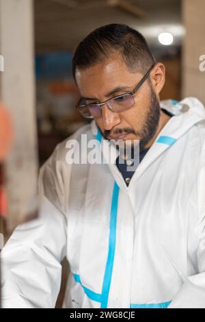 face of young latin man with beard wearing white overalls with glasses and focused while working, person Stock Photo