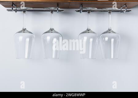 Four sparkling wine glasses hang from a wooden rack against a white wall, showcasing a clean and modern kitchen storage solution. Stock Photo