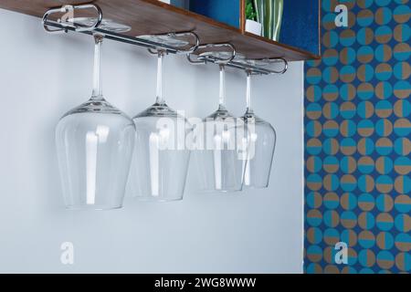 rystal wine glasses hang from a wooden rack. patterned retro wallpaper on the wall Stock Photo