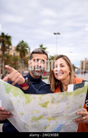 Middle-aged happy Caucasian couple holding travel map looking and pointing tourist interest places. Stock Photo