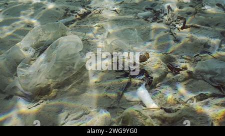 Plastic garbage lies on sandy-silty bottom of sea in shallow water on bright sunny day in sun glare. Seabed polluted with plastic and other debris Stock Photo
