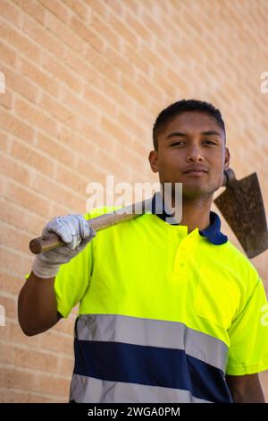 Vertical portrait of a latin man in work clothes holding a sickle on his shoulder and looking at the camera Stock Photo