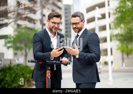 Businessmen using mobile phone outdoor. Confident mature businessman talking on mobile phone while walking outside. Business men looking at messages Stock Photo