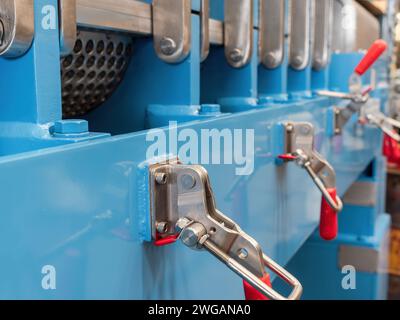 Locking clamps on an industrial twin screw press. Shallow depth of field with the nearest clamp in focus. Stock Photo