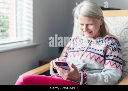 A hard working self-employed female,sits in an armchair,in her house,using a mobile phone to leisurely chat to an old friend, and takes time to relax, Stock Photo