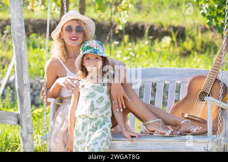Happy mother and child swinging outdoor. Young mother with little kid son sitting on swing in summer park. Mothers day. Happiness, loving family and Stock Photo