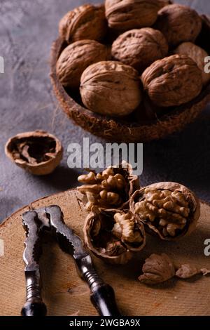 on a wooden disc some kernels in the foreground and an old nutcracker. A bowl with the whole walnuts aside. Stock Photo