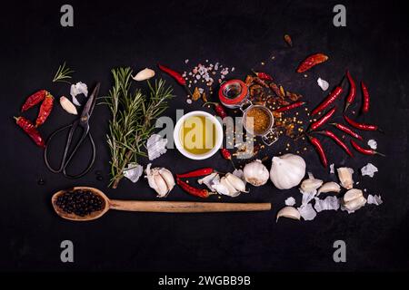 sprigs of rosemary, a metal scissor, a bowl with olive oil, juniper berries and various spices in the foreground, on a textured black background. View Stock Photo