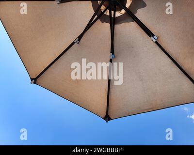 Low angle view of an opened beach fabric umbrella against the blue sunny sky, view from under parasol, holiday or vacation concept, with copy space Stock Photo