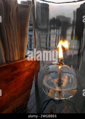 Oil lantern desk lamp, transparent glass, romantic light on the wooden table, warm mood restaurant, close up, dining table setting with tissue paper Stock Photo