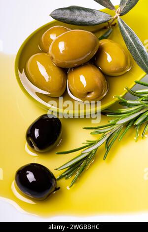 in the foreground, in a green ladle, there are olives with extra virgin olive oil flavored with rosemary Stock Photo