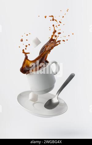 coffee poured from a floating cup with a teaspoon and sugar cubes isolated on white background Stock Photo