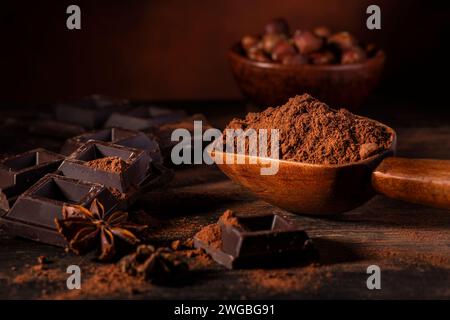 in the foreground, in a dark environment, cocoa powder, pieces of dark chocolate and hazelnuts Stock Photo