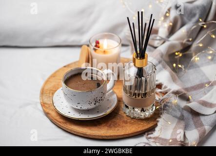 Bamboo sticks in bottle with scented candles and cup of coffee on the bed. Cozy atmosphere concept. Stock Photo
