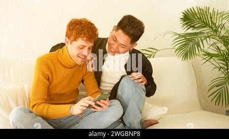 Gay couple smiling while using the mobile at home Stock Photo