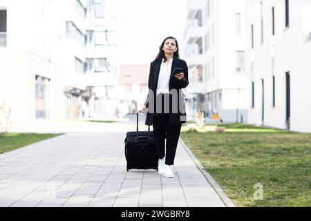 Woman walking past an apartment building pulling wheeled luggage, Germany Stock Photo