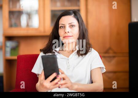 Woman sitting on a chair at home using a mobile phone Stock Photo