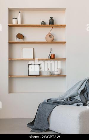 Cosy armchair with a blanket in a living room next to shelves with assorted photo frames, vases and assorted ornaments Stock Photo