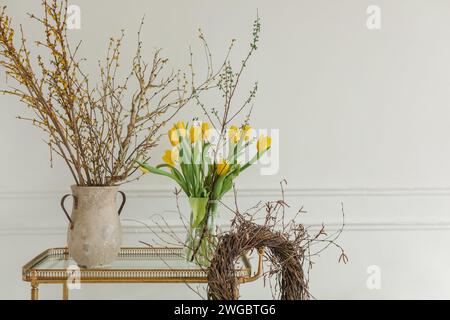 Close-up of a bunch of yellow tulips in a vase on a table with a rustic wreath and jug with branches Stock Photo