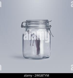 Scared young woman trapped in a huge glass jar, she is lonely and hopeless Stock Photo
