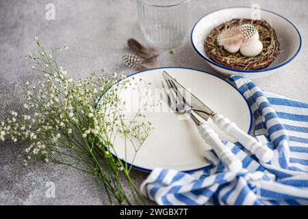 Easter place setting with  white gypsophila flowers and a bird's nest with painted Easter eggs and feathers Stock Photo