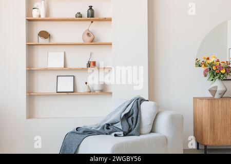 Cosy armchair with a blanket in a living room next to shelves with assorted photo frames, vases and assorted ornaments Stock Photo