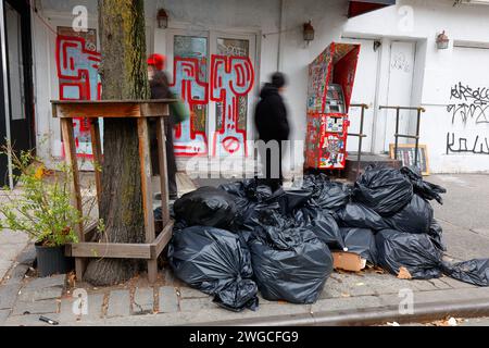 People walk past garbage bags, and a closed business vandalized with graffiti, in Manhattan's East Village, New York City, January 2024. Stock Photo