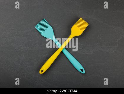 Two silicone brushes for pastry or basting on black slate board with copy space, colorful modern culinary kitchen utensils, close up, elevated table t Stock Photo