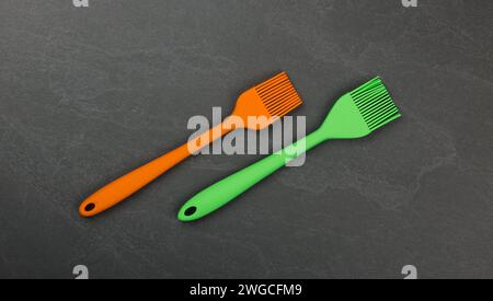 Two silicone brushes for pastry or basting on black slate board with copy space, colorful modern culinary kitchen utensils, close up, elevated table t Stock Photo