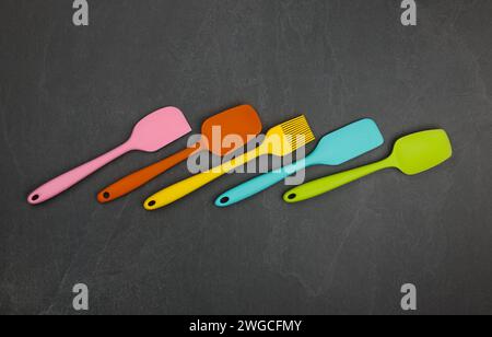 Five silicone cooking spatulas and brushes on black slate board with copy space, colorful modern culinary kitchen utensils, close up, elevated table t Stock Photo