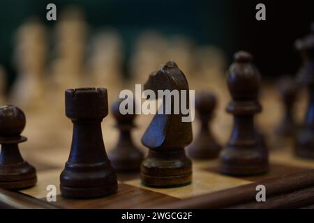 A black and white chess pieces arranged on a wooden table, juxtaposed against a wall Stock Photo