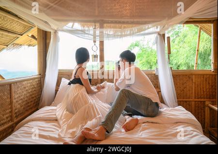 Happy young asian couple enjoying and taking photo nature view with retro camera inside of wooden hut among the forest on honeymoon vacation Stock Photo
