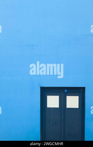 Blue Double Doors Set Into A Blue Painted Concrete Wall, UK Stock Photo