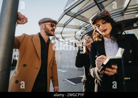 Three young entrepreneurs engage in a collaborative effort using a smart phone under the urban sun. A modern approach to business on the move. Stock Photo
