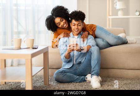 A relaxed and happy young couple lounges on the floor, leaning against a sofa Stock Photo